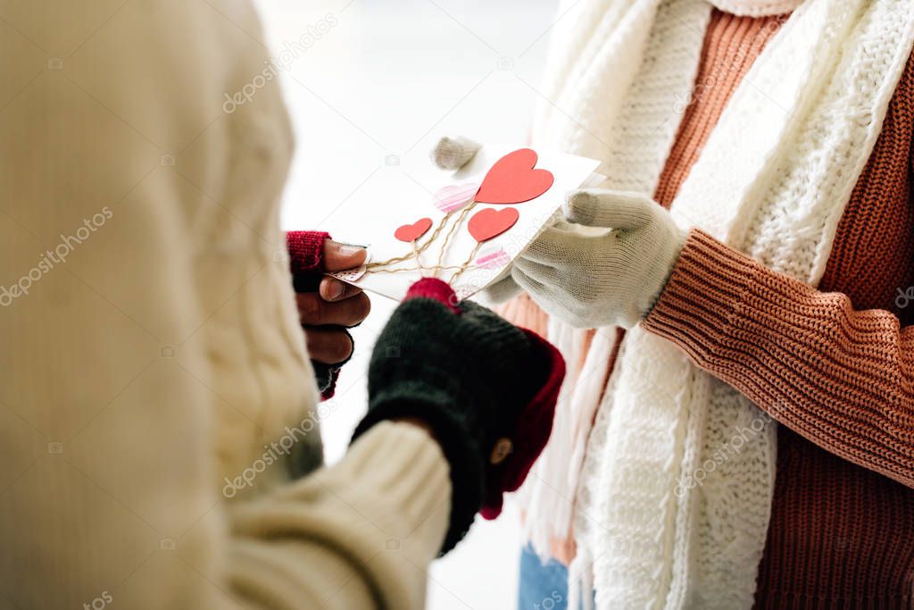 cropped view of man giving greeting card with hearts on valentines day to woman on skating rink