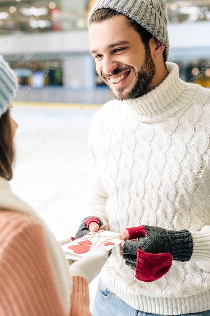 happy man giving greeting card on valentines day to woman on skating rink
