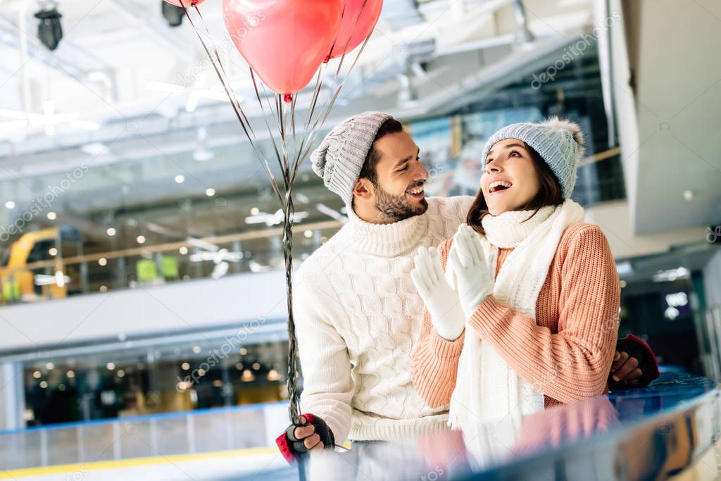 excited couple with red heart shaped balloons spending time on skating rink on valentines day