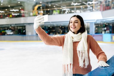 Neşeli kız buz pateni pistinde akıllı telefondan selfie çekiyor.