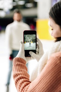 Paten sahasında akıllı telefondan erkeğin fotoğrafını çeken seçici bir kadın.