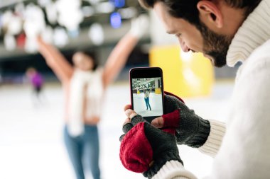 Gülümseyen adamın akıllı telefondan buz pateni pistinde bir kadının fotoğrafını çekmesi.