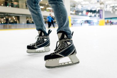 cropped view of man in jeans and skates standing on skating rink clipart