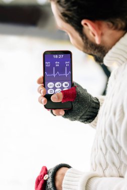 Kyiv, Ukrayna - 15 Kasım 2019: Eldivenli bir adamın ekranda sağlık uygulamalı akıllı telefon ile buz pateni pistinde görüntüsü