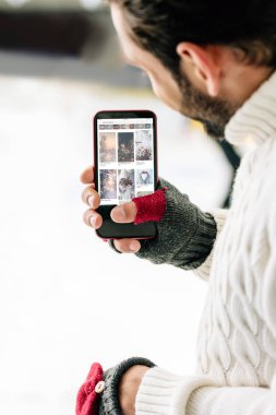 Kyiv, Ukrayna - 15 Kasım 2019: Pinterest uygulamalı akıllı telefon tutan eldivenli adamın ekranda, buz pateni pistinde görüntüsü