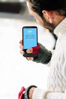 Kyiv, Ukrayna - 15 Kasım 2019: Eldivenli bir adamın Skype uygulamalı akıllı telefonu ekranda, buz pateni pistinde görüntüsü