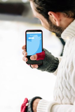 Kyiv, Ukrayna - 15 Kasım 2019: eldivenli bir adamın twitter uygulamalı akıllı telefonunu ekranda, buz pateni pistinde tutuşu
