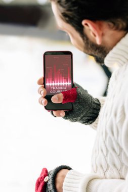 Kyiv, Ukrayna - 15 Kasım 2019: Eldivenli adam ekranda, buz pateni pistinde akıllı telefon ile ticaret uygulaması tutuyor.
