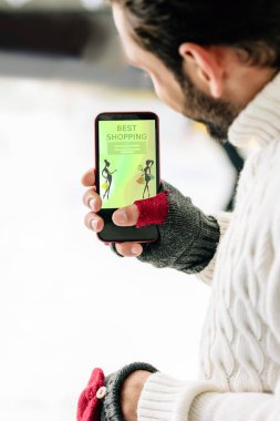 Kyiv, Ukrayna - 15 Kasım 2019: En iyi alışveriş uygulaması ekranda, buz pateni pistinde akıllı telefon tutan eldivenli adam görüntüsü