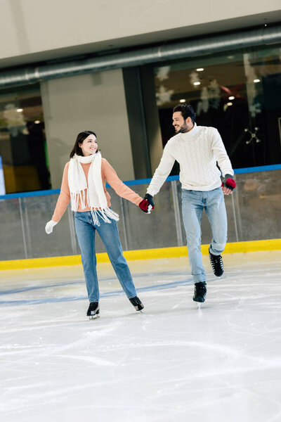 young couple holding hands and skating on rink  