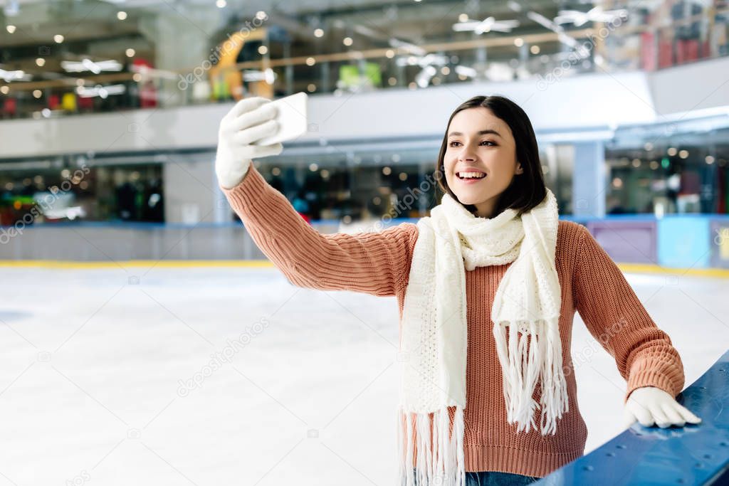 cheerful girl taking selfie on smartphone on skating rink
