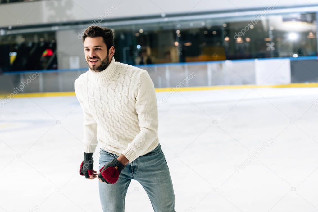 handsome man in jeans and sweater skating on rink