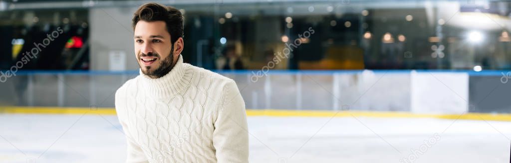 panoramic shot of handsome smiling man in jeans and sweater skating on rink