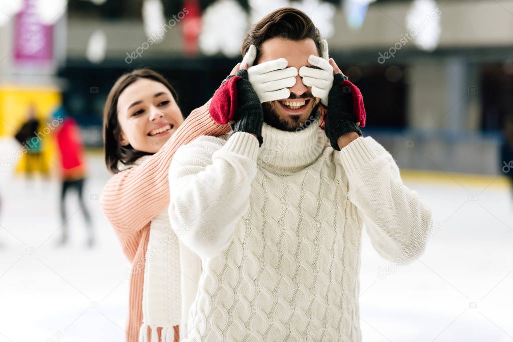 happy girl closing eyes to smiling man to make a surprise on skating rink  