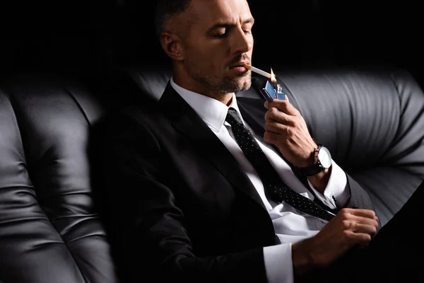 Uomo Affari Accensione Sigaretta Mentre Seduto Sul Divano Isolato Nero — Foto Stock