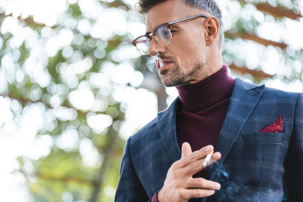 Low angle view of confident businessman smoking cigarette outdoors