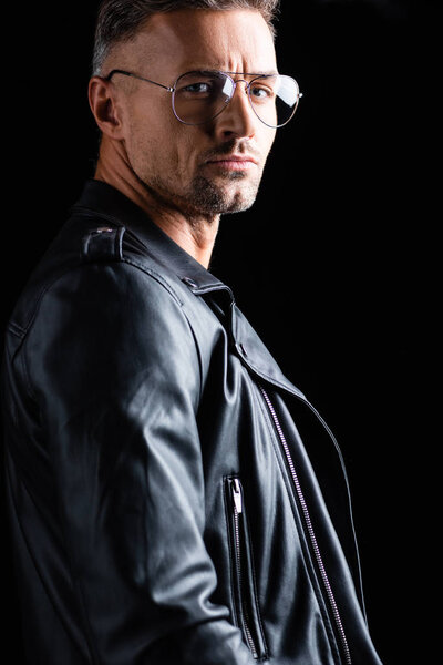 Side view of handsome man in leather jacket looking at camera isolated on black 