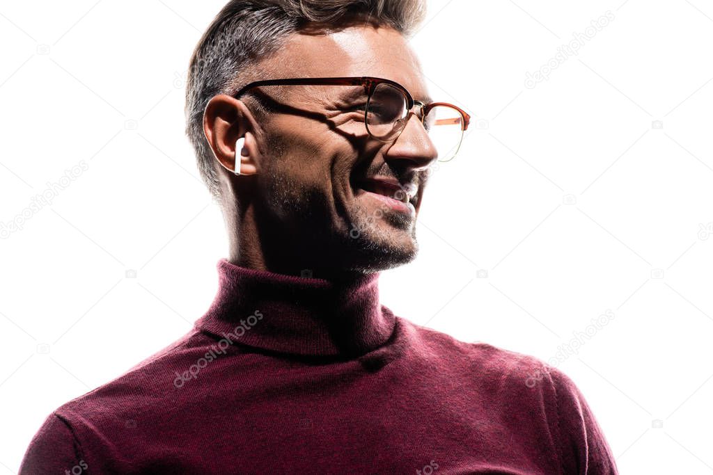 Smiling man in wireless earphones and eyeglasses looking away isolated on white