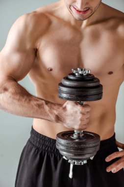 partial view of sexy muscular bodybuilder with bare torso exercising with dumbbell isolated on grey clipart