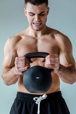 Gergin, seksi kaslı vücut geliştirici. Vücut egzersizi yapıyor. Gri tenli, kettlebell kullanıyor.