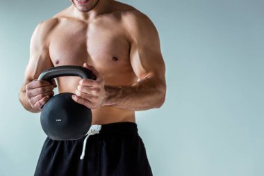 Çıplak vücut egzersizi yapan seksi kaslı vücutçunun kısmi görüntüsü gri tenli kettlebell ile izole edilmiş.