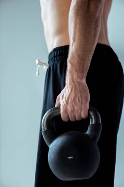 Gri renkli kettlebell ile egzersiz yapan seksi kaslı vücutçunun kısmi görüntüsü