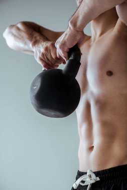 Çıplak gövde egzersizi yapan seksi kaslı vücutçunun gri üzerinde izole edilmiş kettlebell ile görüntüsü.
