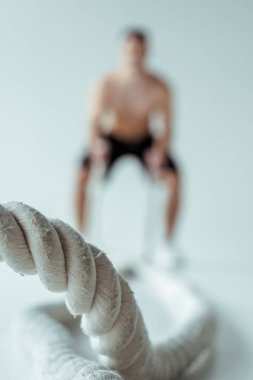 Gri arka planda savaş halatıyla egzersiz yapan adamın seçici odak noktası