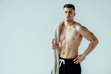 Çıplak gövdeli seksi kaslı vücut geliştirici. Gri üzerinde izole edilmiş savaş halatıyla poz veriyor.