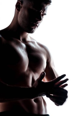 Çıplak gövdeli seksi kaslı vücut geliştirici. Beyaz tenli gölgede poz veriyor.