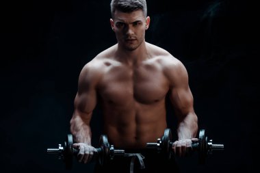 sexy muscular bodybuilder with bare torso excising with dumbbells isolated on black clipart