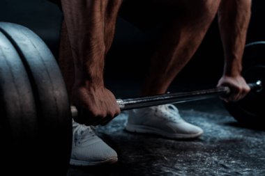 Siyah arka planda halterle kesilen kaslı vücut geliştirici görüntüsü