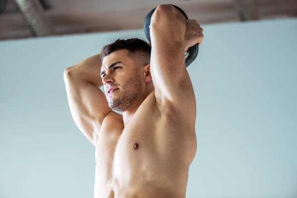 low angle view of sexy muscular bodybuilder with bare torso exercising with kettlebell