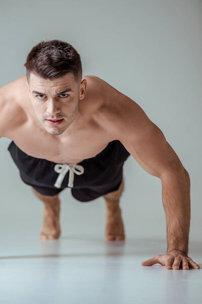 сексуальный мускулистый спортсмен с голым туловищем, отжимающийся на сером
