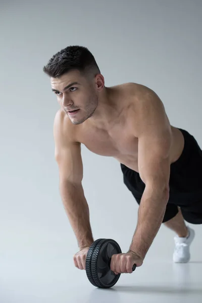 Sexy muscular bodybuilder with bare torso exercising with ab wheel on grey background — Stock Image Sexy Muscular Bodybuilder Bare Torso Exercising Wheel Grey Background Stock Picture