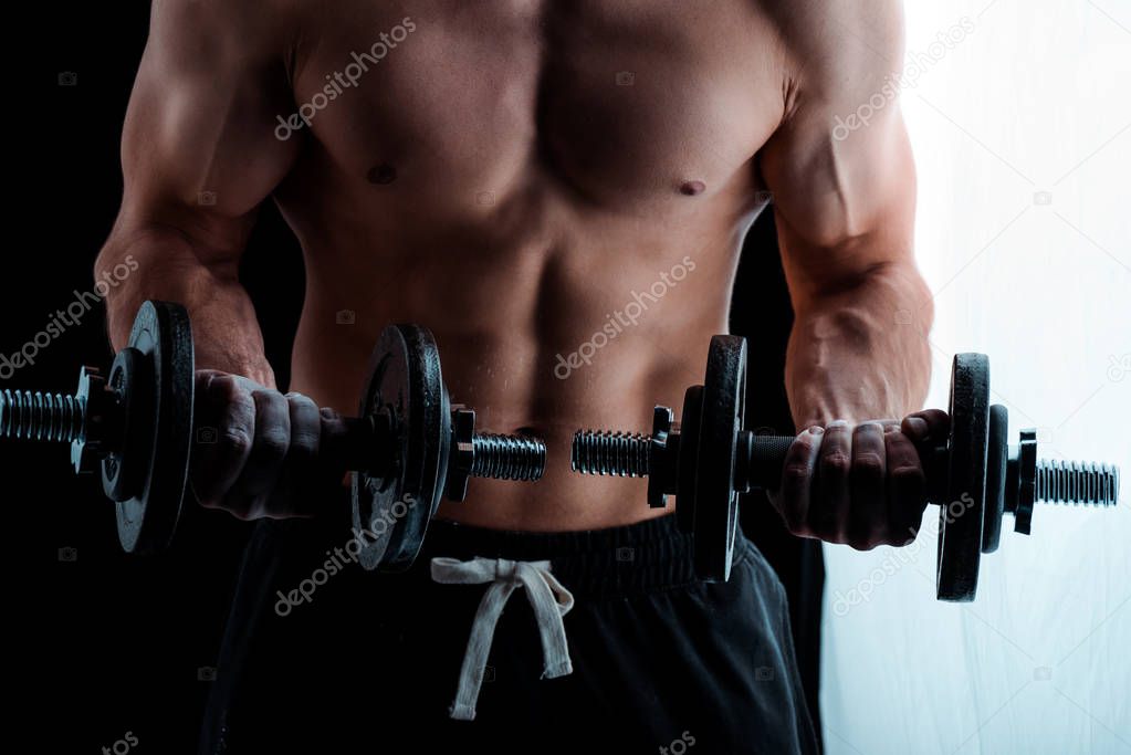 cropped view of sexy muscular bodybuilder with bare torso exercising with dumbbells