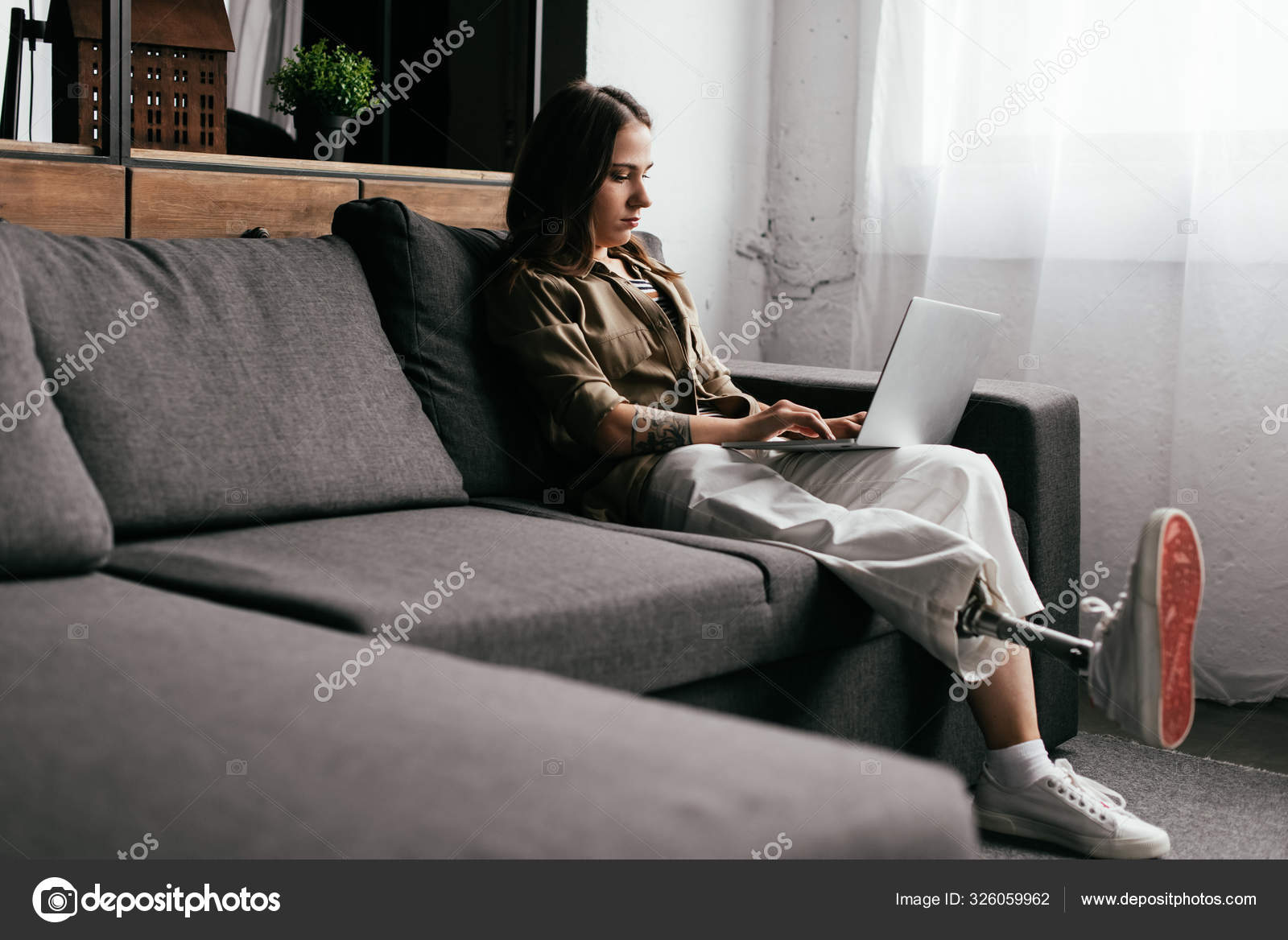 Smiling Young Woman With Prosthetic Leg Using Laptop In Living