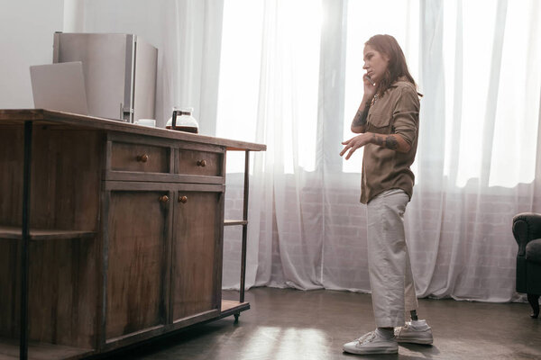 Вид сбоку на молодую женщину с протезной ногой, разговаривающую на смартфоне дома
