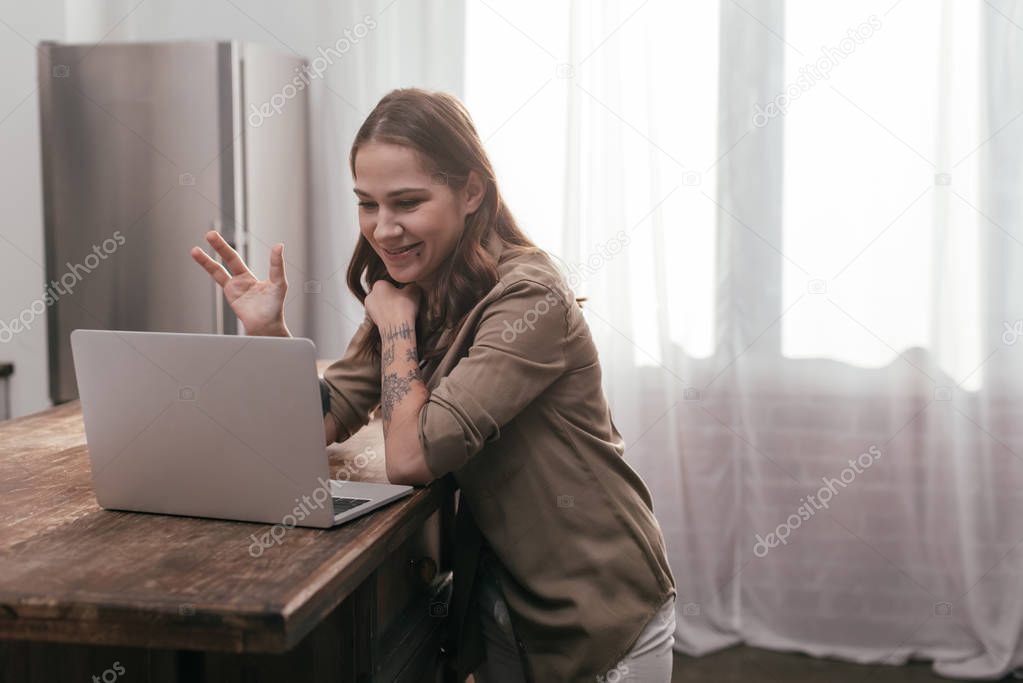 Beautiful smiling girl having video chat on laptop by kitchen table