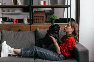 Oturma odasında kanepede köpeğiyle oynayan protez bacaklı genç bir kadın. 