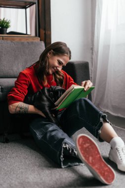 Protez bacaklı gülümseyen kız kitap okuyor ve evde yerde pug 'a sarılıyor.