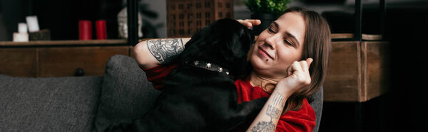 Панорамный снимок красивой девушки, играющей с собакой-мопсом на диване
