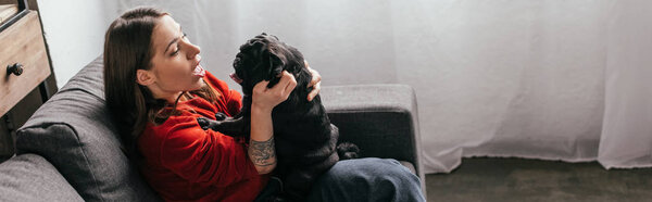 Вид сбоку молодой женщины, играющей с мопсом, панорамный снимок
