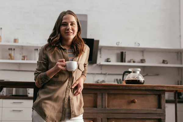 Güzel Bir Kız Kahve Fincanı Tutuyor Mutfakta Kameraya Gülümsüyor — Stok fotoğraf