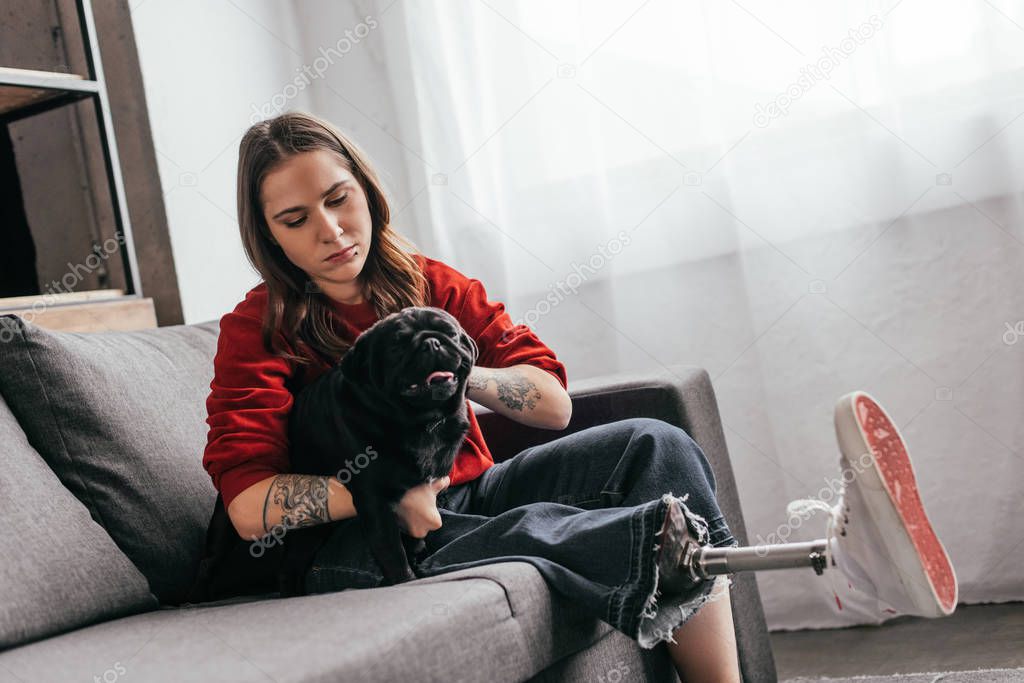 Woman with leg prosthesis stroking pug on sofa