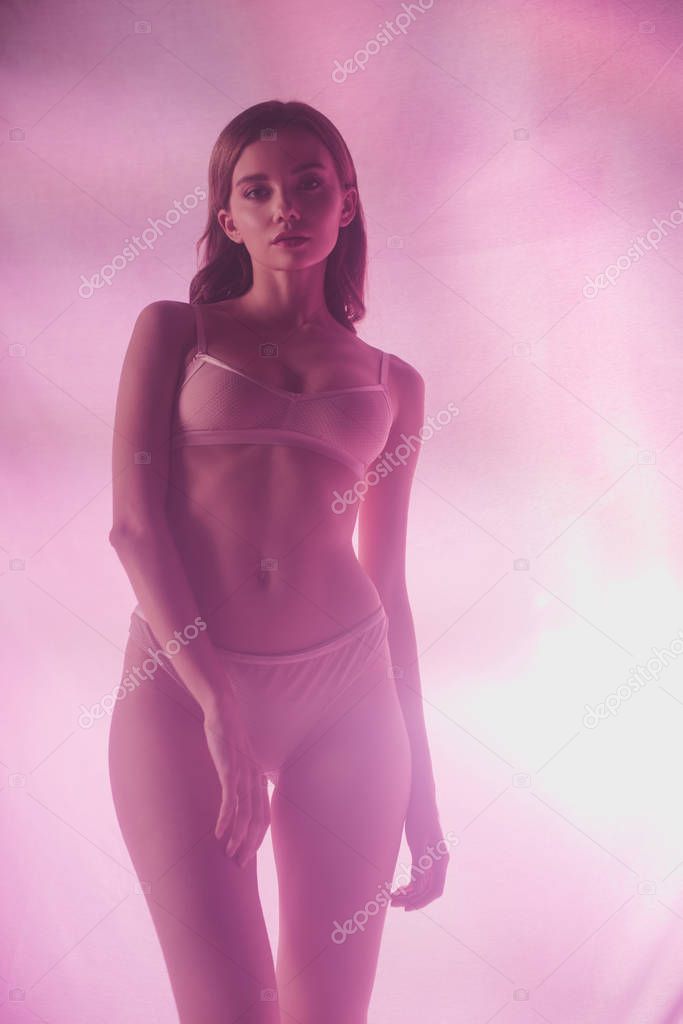 sensual girl in lingerie looking at camera while posing on pink and purple background with lighting