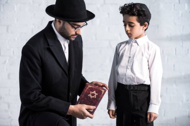 handsome jewish father holding tanakh and cute son looking at it  clipart