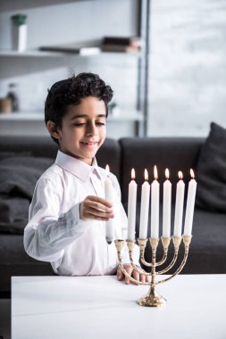 Şirin ve gülümseyen, tişörtlü, elinde mum tutan Yahudi çocuk. 