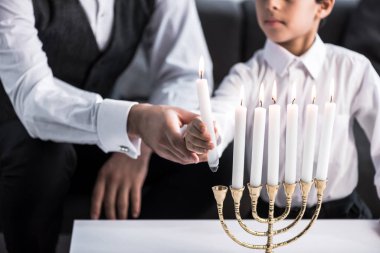 cropped view of jewish father and son holding candle in apartment  clipart