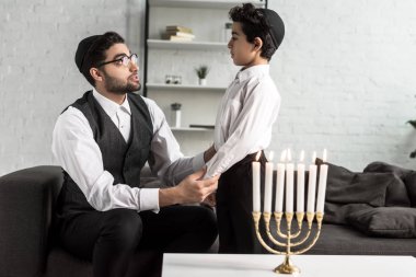 jewish father and cute son holding hands in apartment  clipart